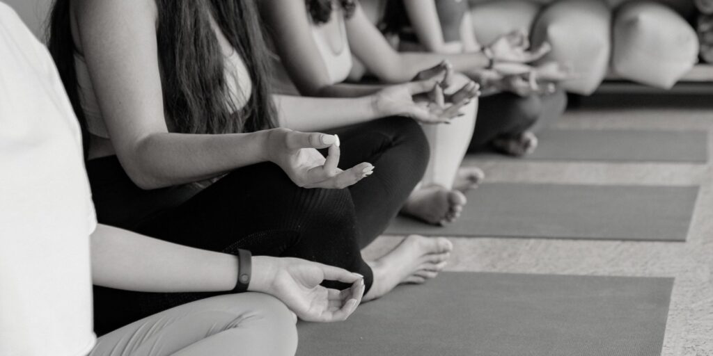 Man sieht eine Reihe Menschen in Yoga Kleidung während einer Entspannungsübung